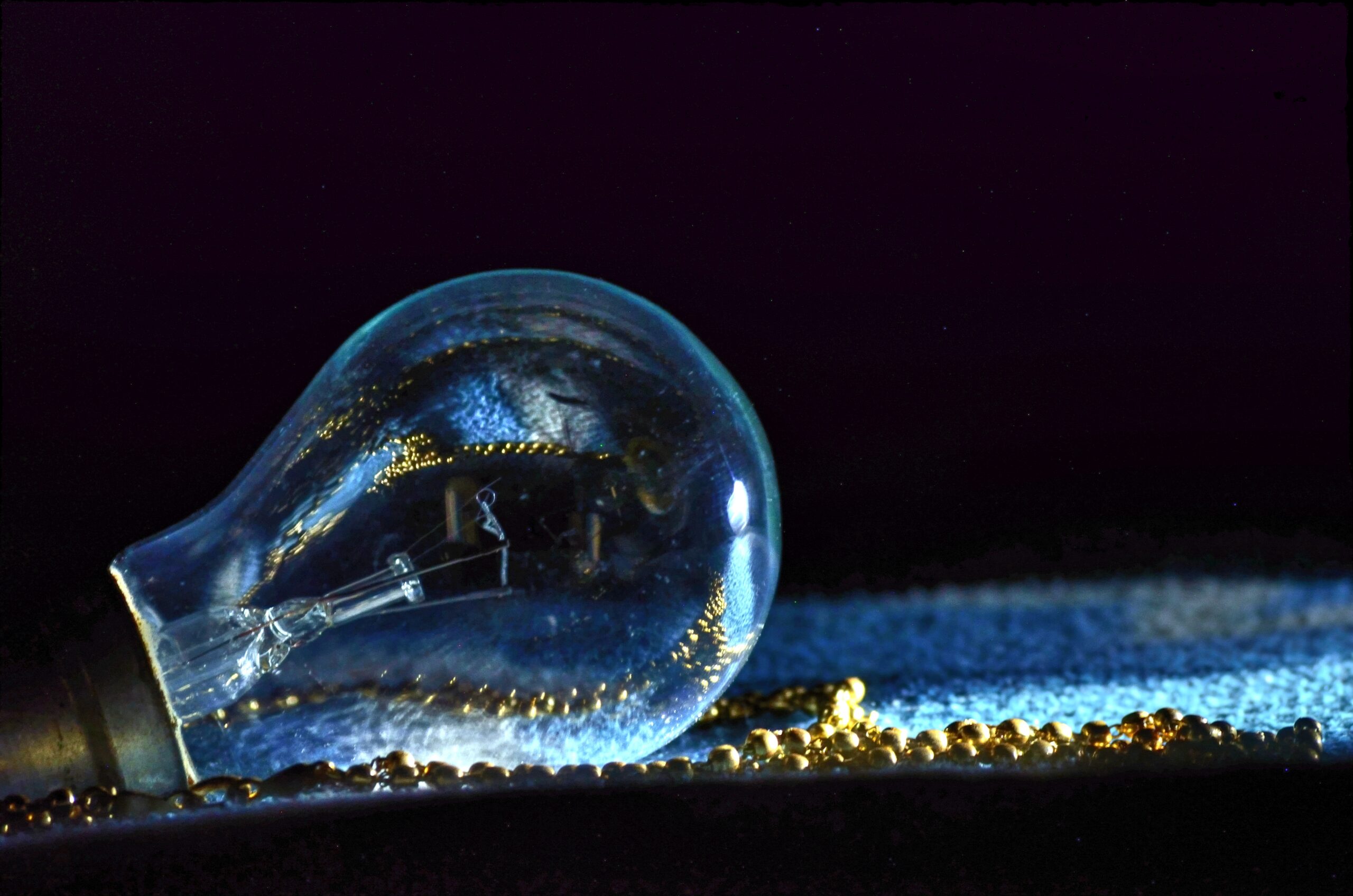 Closeup shot of aincandescent lamp with blue light and reflecting small golden ball on a black color